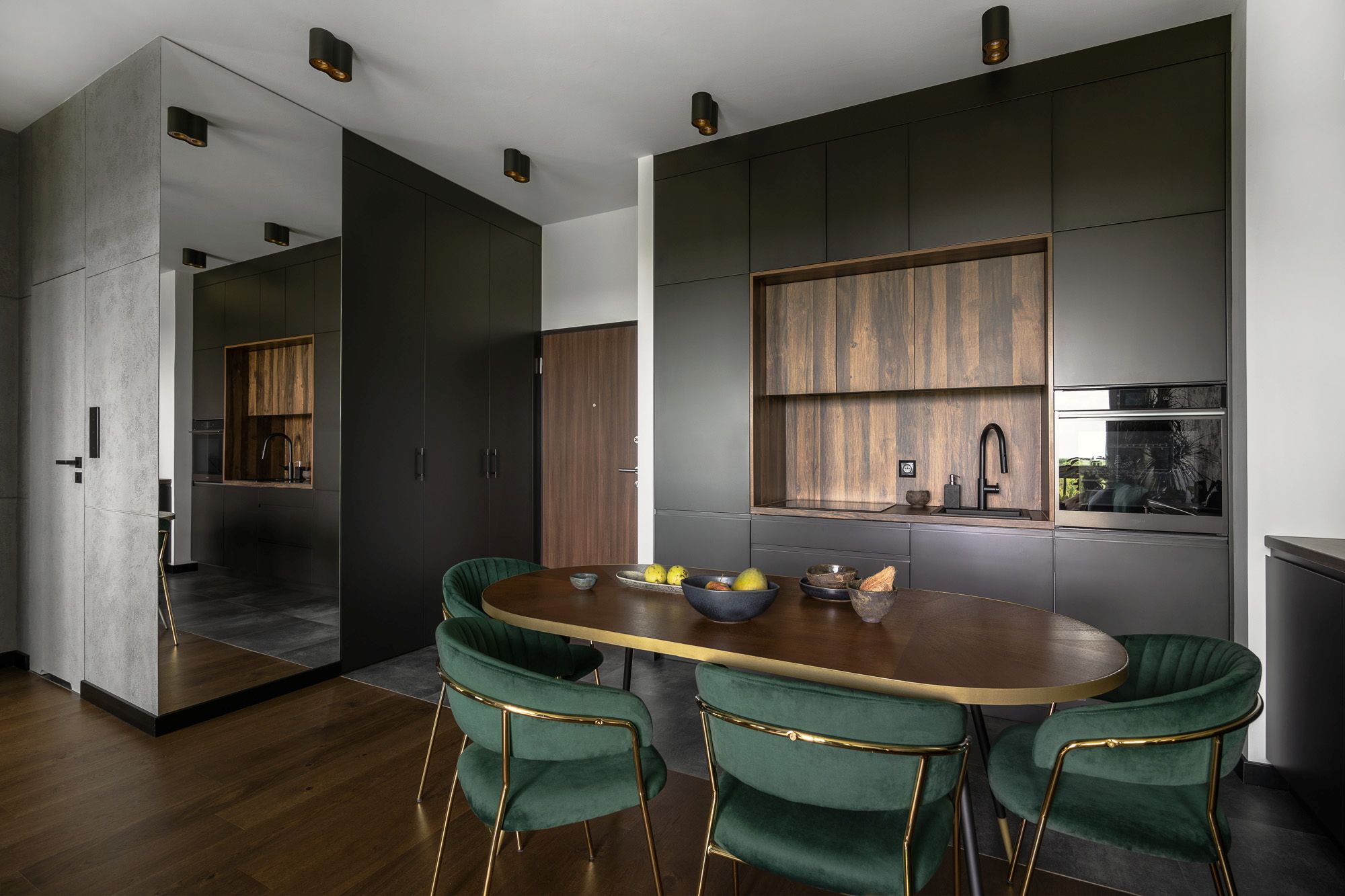 Salon z&nbsp;kuchnią w&nbsp;ciemnej aranżacji z&nbsp;ciemną podłogą i&nbsp;ciemnymi drzwiami wejściowymi.
